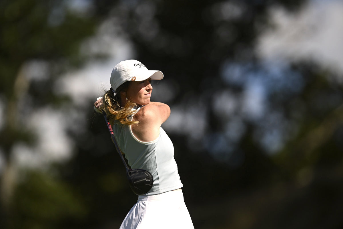 A woman in a white cap follows through on her golf swing
