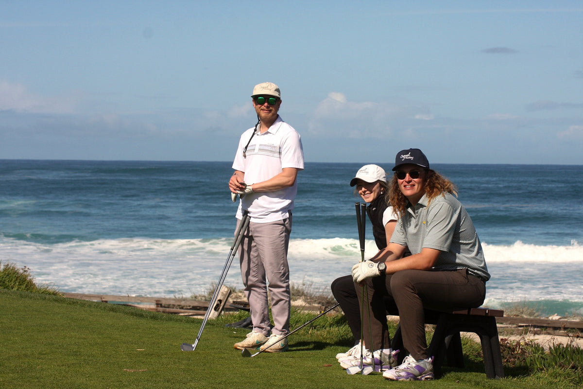 Three friends relax together on a bench overlooking the ocean with their clubs