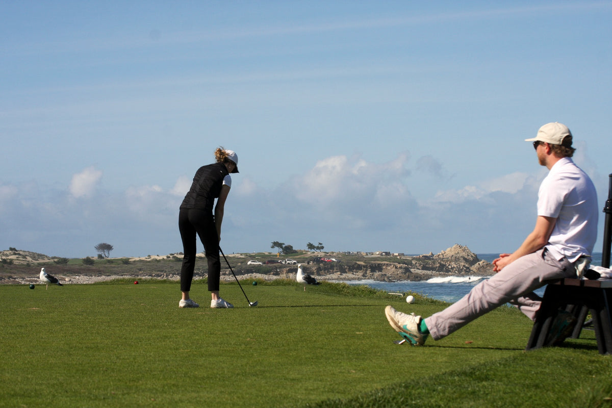 Friends sit together on the tee box while one lines up a shot by the ocean